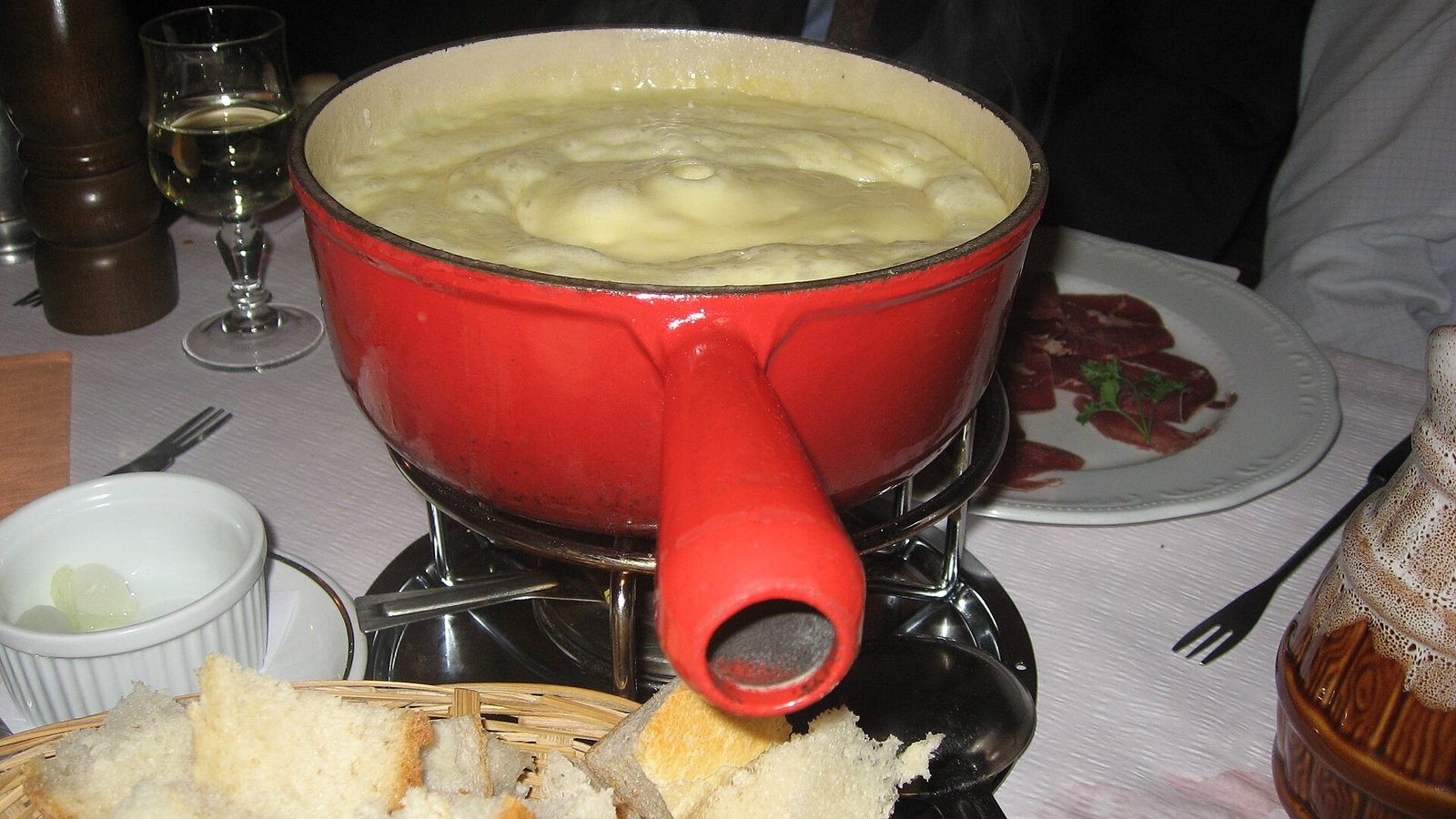 Fondue history: a red caquelon of bubbling Swiss cheese fondue with a basket of bread cubes