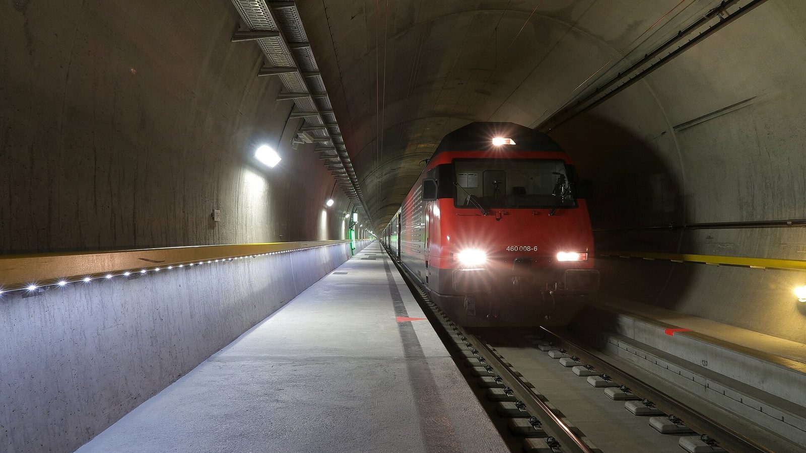 Gotthard Base Tunnel: an SBB passenger train with headlights emerging inside the lit tunnel tube
