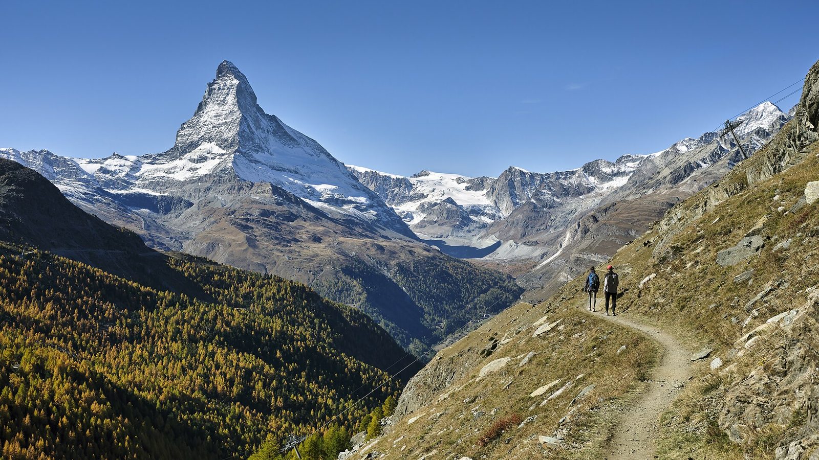 The Matterhorn above Zermatt in autumn, with hikers on a mountain trail and golden larch forests