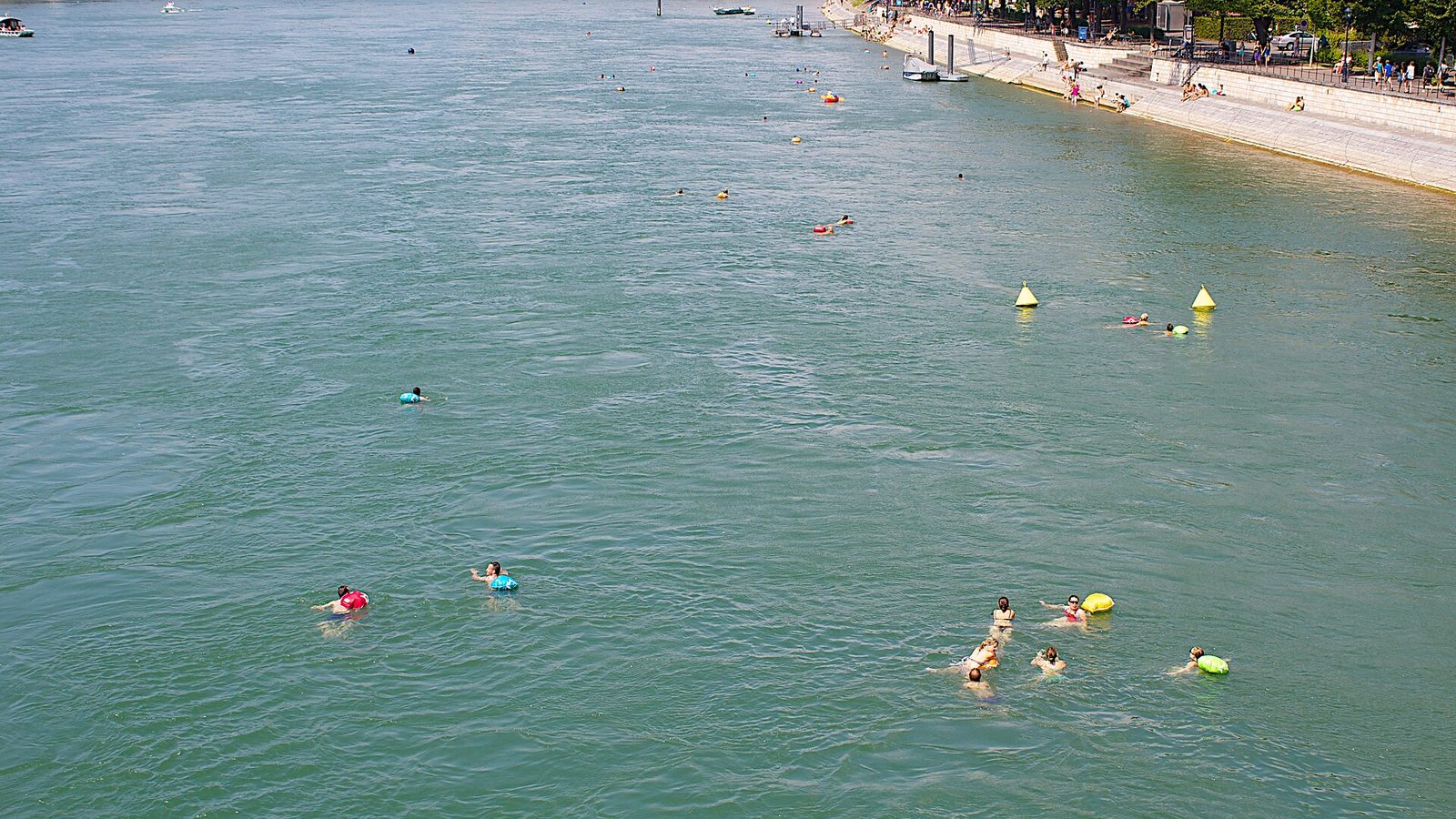 River swimming in Switzerland: swimmers with colourful dry bags floating down the Rhine in Basel