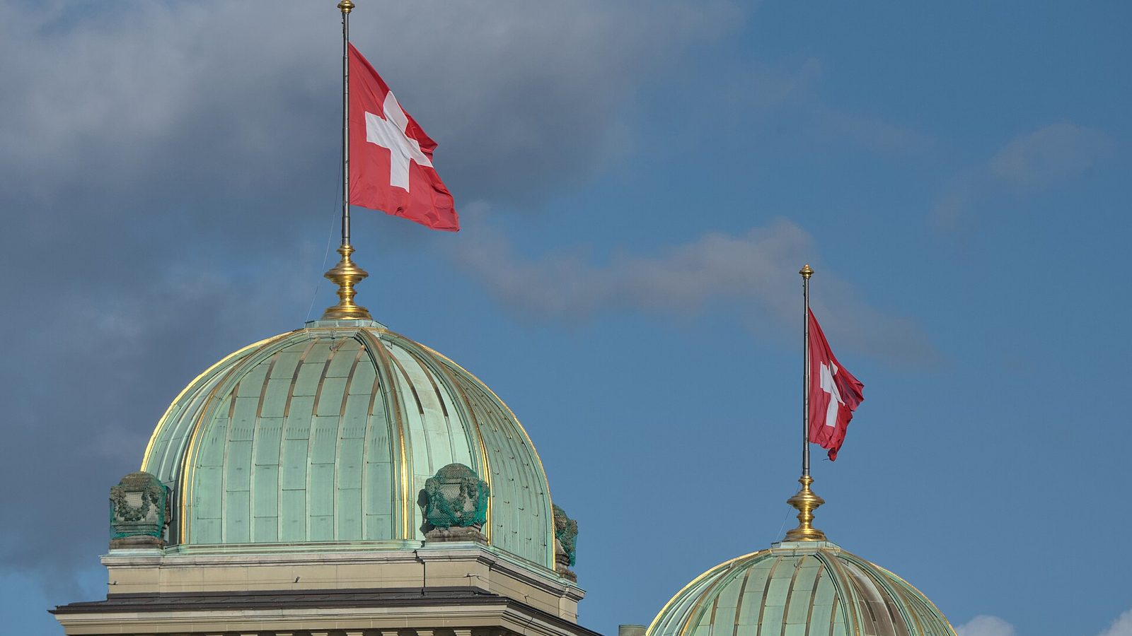 Square Swiss flag flying above the copper domes of the Federal Palace in Bern