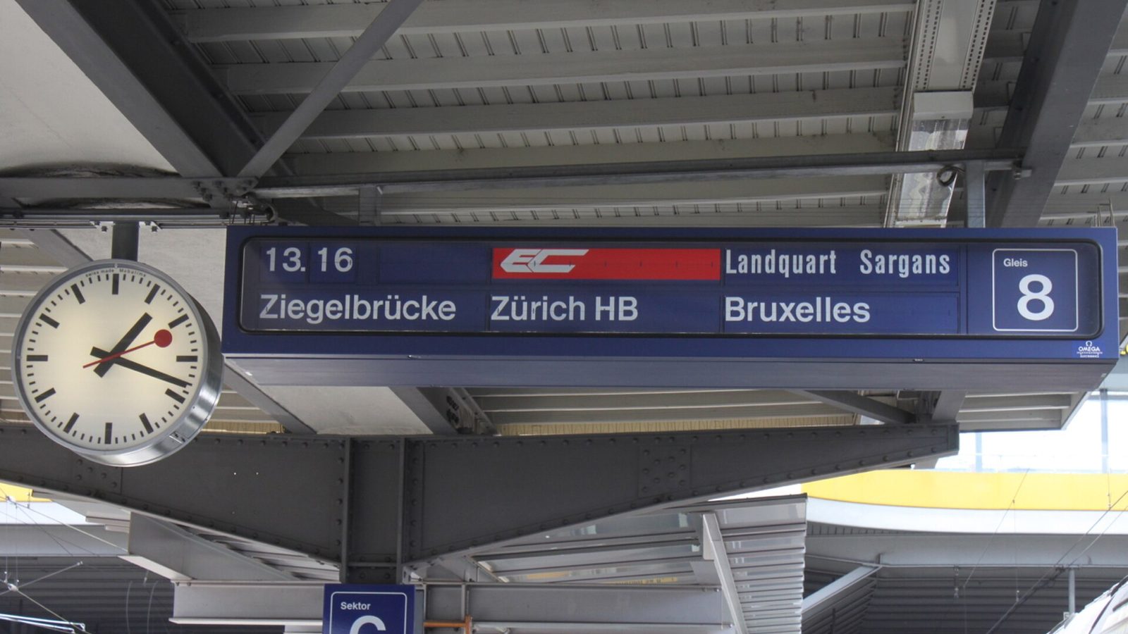 Swiss railway clock next to a split-flap departure board at Chur station showing a EuroCity train to Zurich and Brussels
